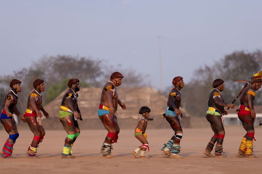 A group of Indigenous Brazilian men and one child perform a traditional dance, moving in in a line.