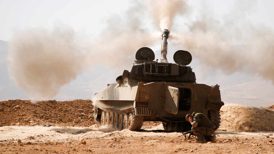 A Hezbollah fighters kneels next to a tank after firing his weapon in Syria