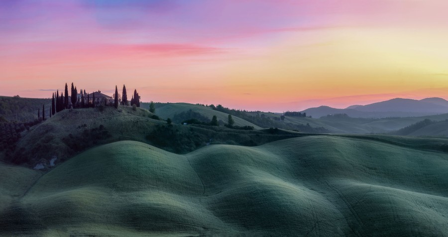 A sunrise view of rolling hills in a Tuscan landscape.