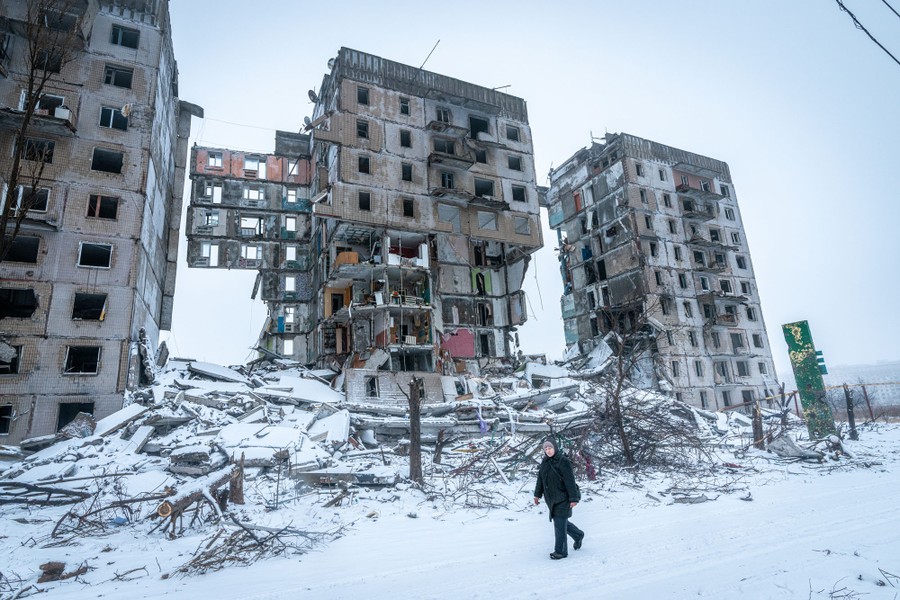 A person walks past a partially collapsed residential building.