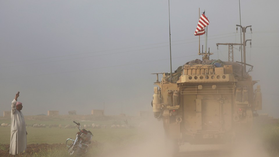 A man gestures at U.S military vehicles near the Turkish border of Syria on April 28, 2017. 