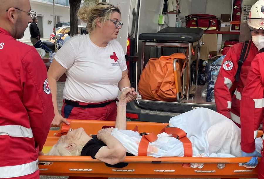 Several health care workers carry an older person on a stretcher.