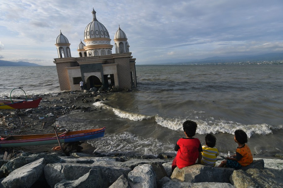 People gather near a damaged mosque on the shore.