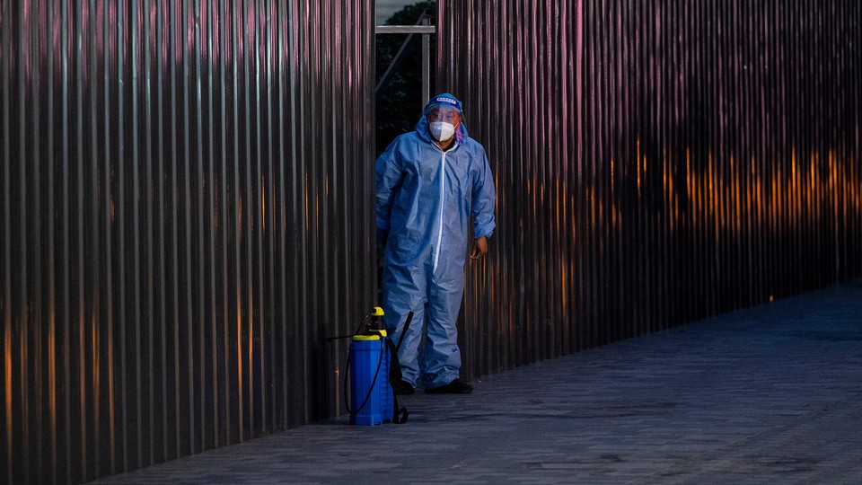 A photo of a Chinese health worker in hazmat suit emerging from behind a fenced enclosure