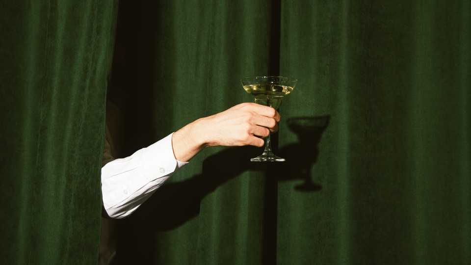 A hand holding a martini glass sticks out from the green curtains