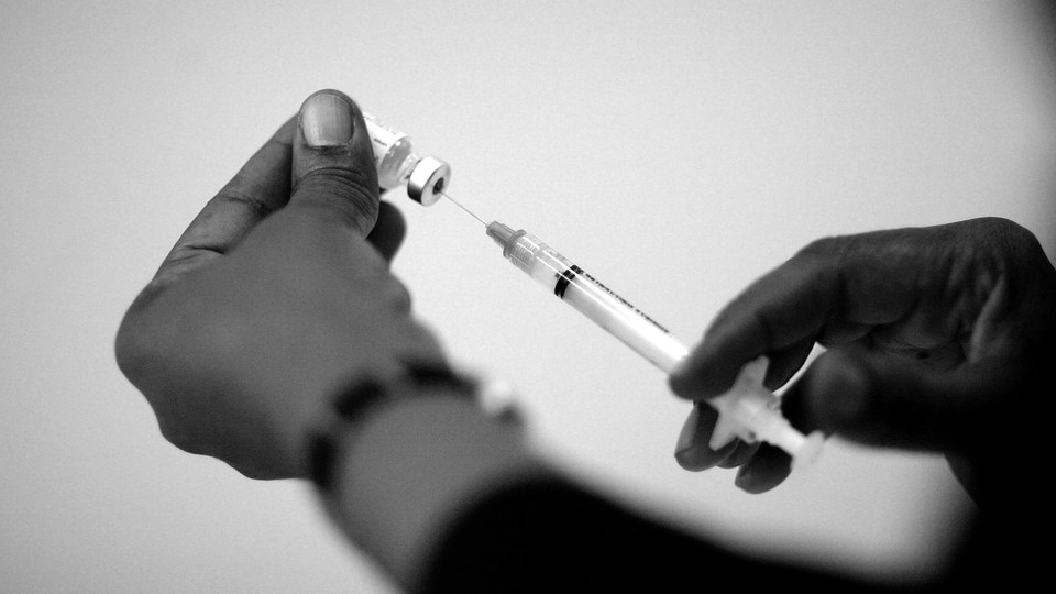 A photo of two hands filling a syringe with a vaccine