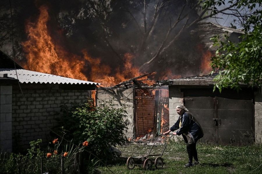 A woman pushes a small cart in front of a residential garage that is going up in flames.