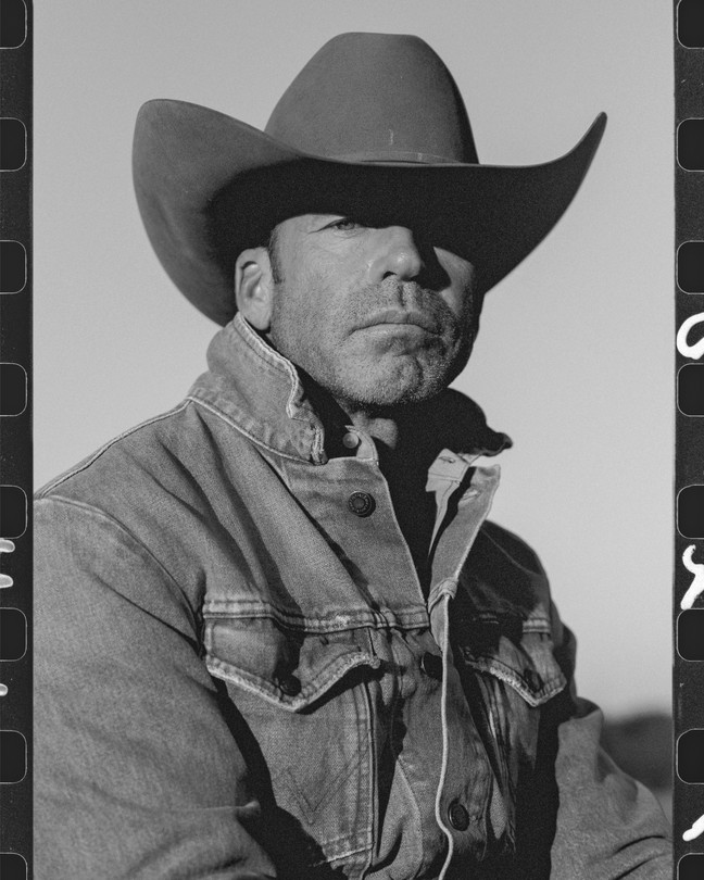 A close up portrait of Taylor Sheridan in cowboy hat with film strip remnants on each side.