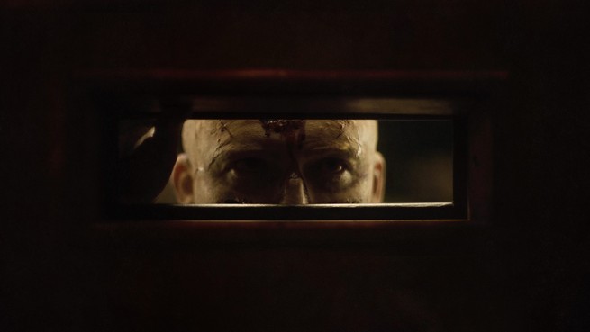Rory Kinnear peering through a slot in a door in "Men"