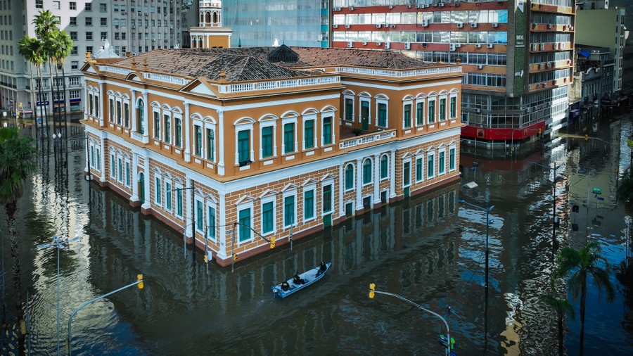 An aerial view of a small boat motoring past a City Hall building on flooded streets