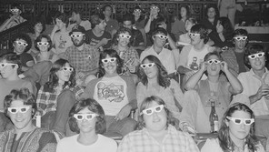Black and white photograph of movie-goers wearing 3D glasses in a theater at a showing.