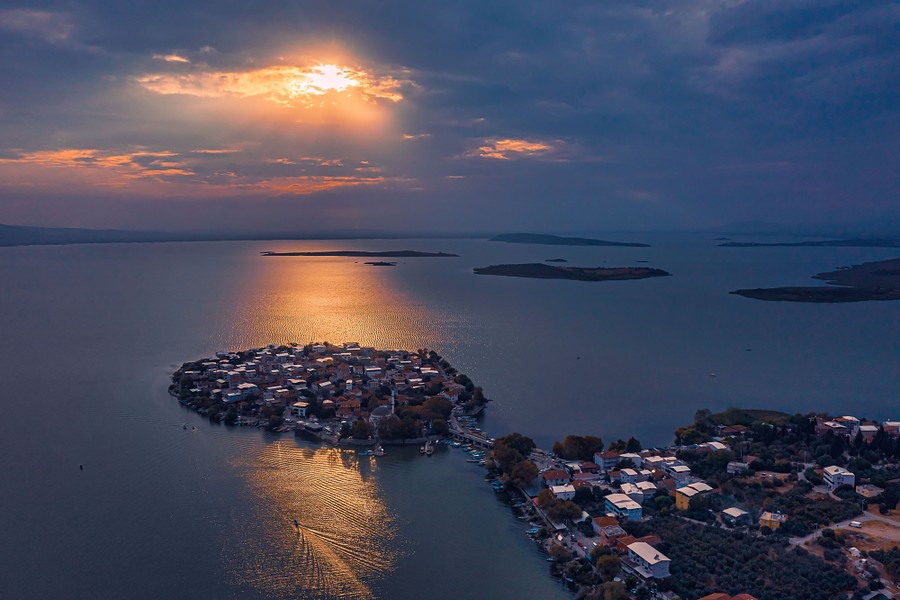 An aerial view of a historic neighborhood on a tiny island-like peninsula in a large lake, at sunset.