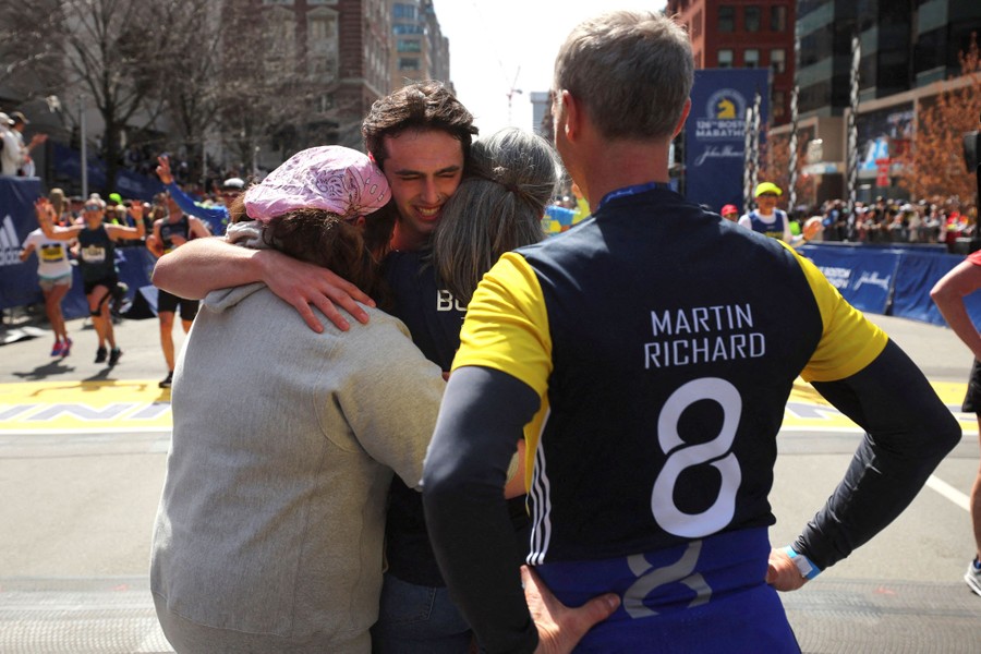 Several people hug while standing in a street at the finish line of a footrace.