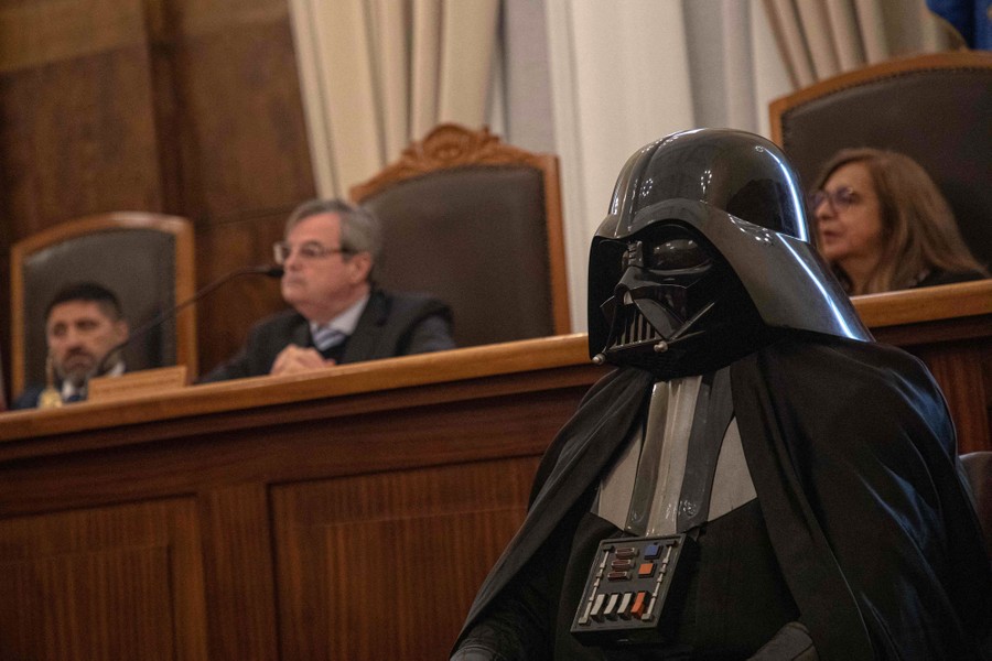 A person in a Darth Vader costume sits before a panel of judges in a courtroom.