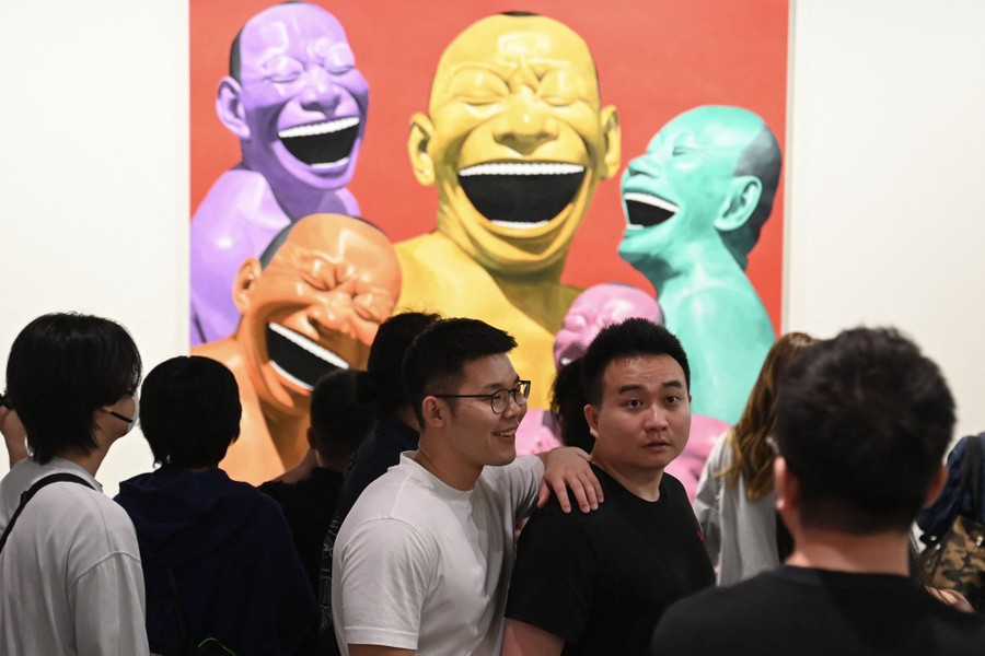 People walk through an exhibition space, looking at artwork, including a painting of caricatures of several colorful smiling men.