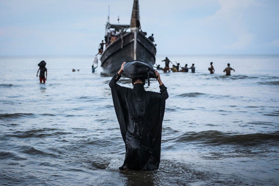 A person walks toward the shore, with a boat floating behind them.