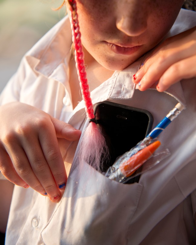 Photograph of a kid with a smartphone and pens in their shirt pocket