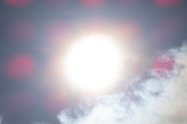 An photo of wispy clouds with a blurry sun, and pink dots across the image