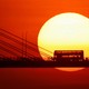 A double-decker bus passes over a bridge, silhouetted at sunset.