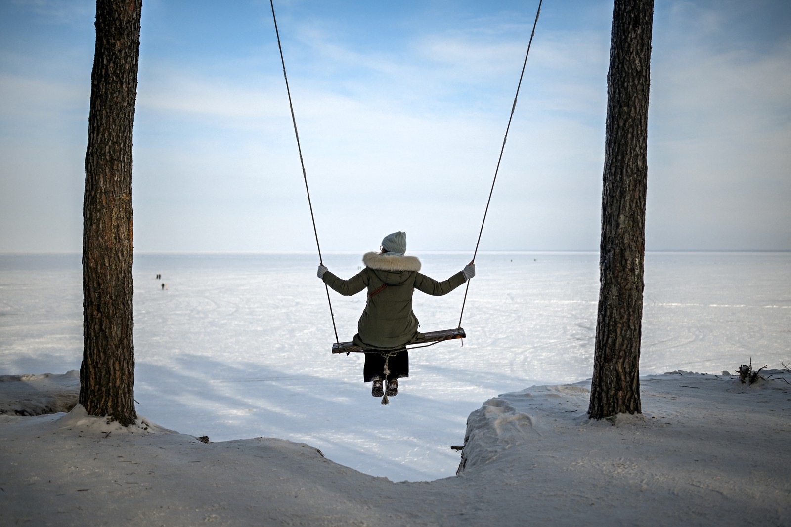 A woman sits on a swing above a frozen reservoir.