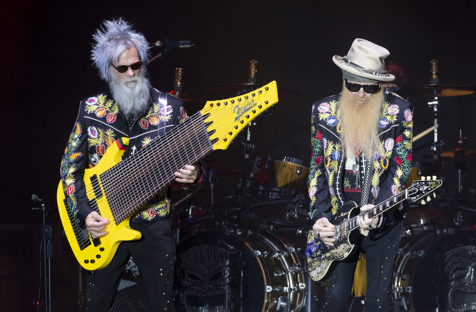 Two musicians perform on stage, with the one at left playing a gigantic 17-string bass guitar.
