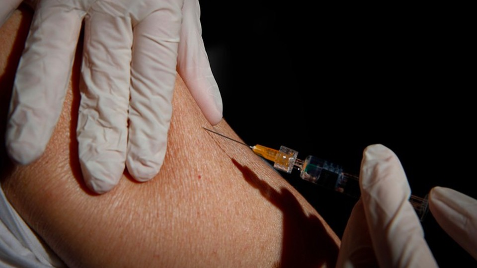 a gloved hand injecting a needle into an arm