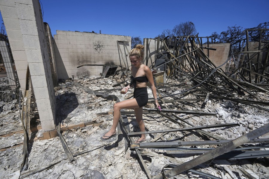 A person walks through the rubble of a burned-down house.