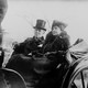 A black-and-white photo of a man in a top hat and a woman riding in a carriage