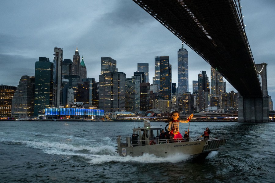 A small boat carries several people and a 12-foot-tall puppet under the Brooklyn Bridge.
