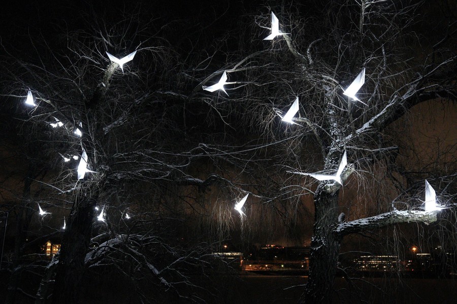 Illuminated birdlike sculptures glow among tree branches.