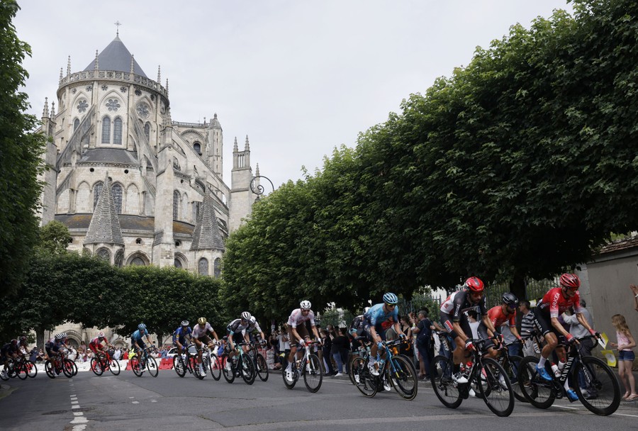 A group of cyclists rides past a large cathedral.