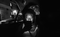 A passenger looks at their phone in the backseat of a dark car.