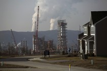 A smoking fracking project sits behind a suburban subdivision and beneath a gray, smoggy sky.