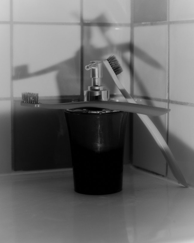 a black and white photo of two toothbrushes leaning against a faucet, their shadows on the tiled wall behind them