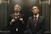 Two men riding in an elevator, staring somewhat skeptically at the ceiling, in "BlackBerry"