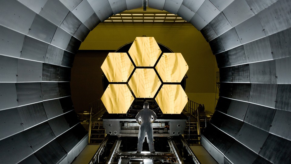 A photograph of a technician looking at the James Webb Space Telescope's gold-covered mirrors