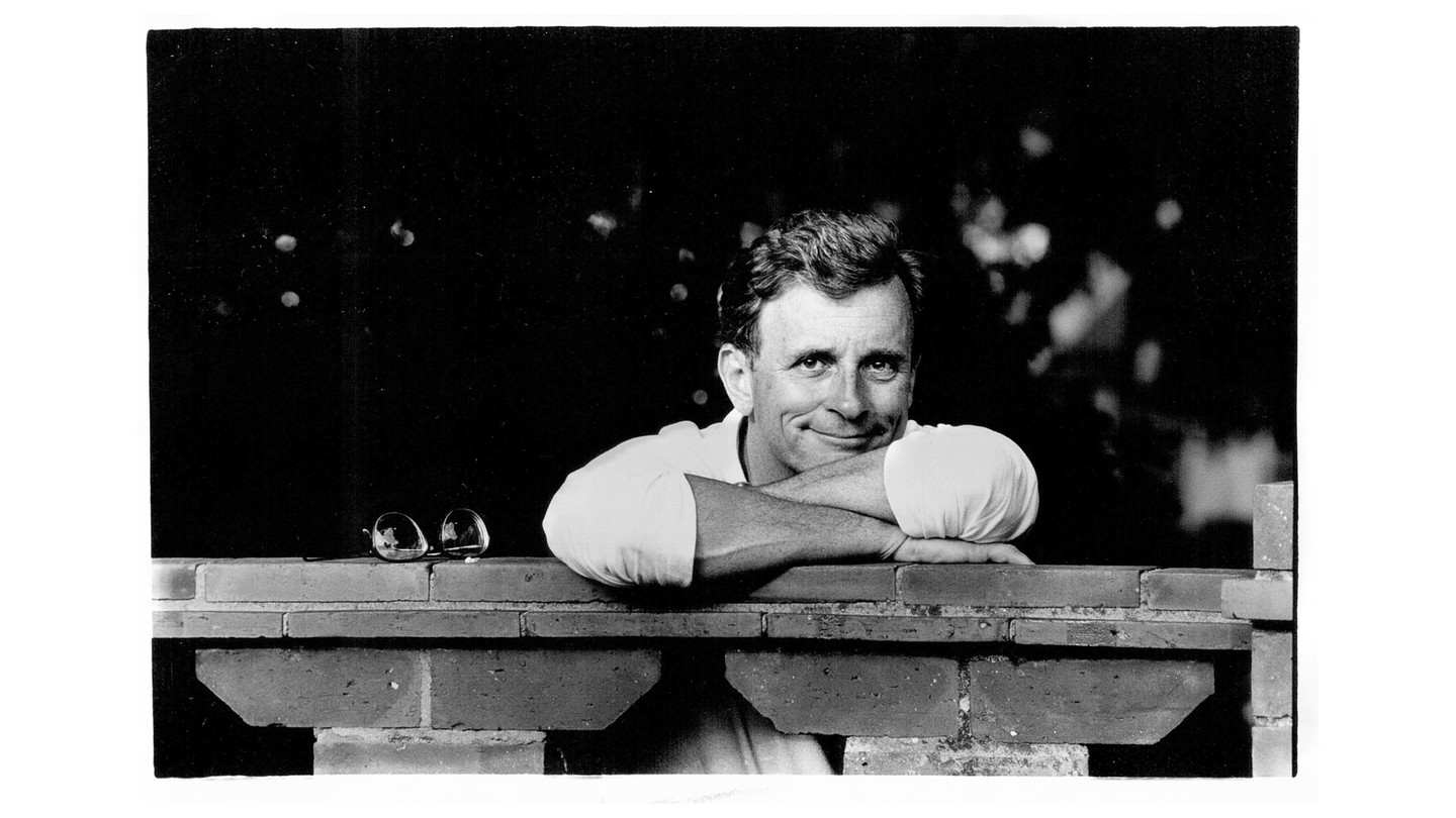 black and white photo of Edmund White smiling, in a white shirt