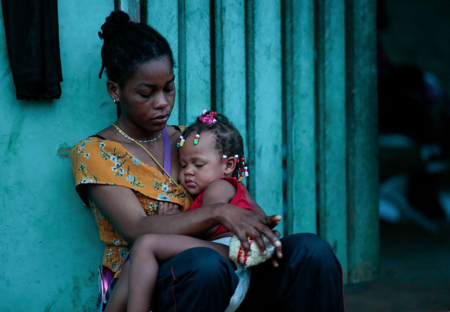 A woman and a child sit together beside a wall.