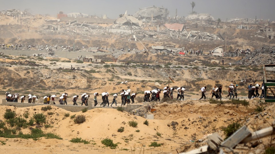 Men carry sacks of flour inside Gaza, where there are ruins in the background