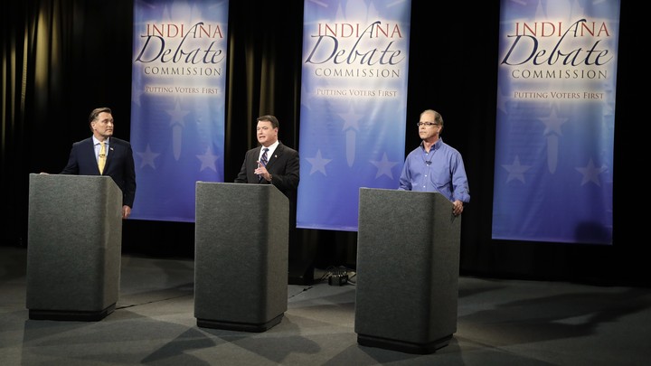 Three senatorial candidates stand at lecterns on a debate stage.