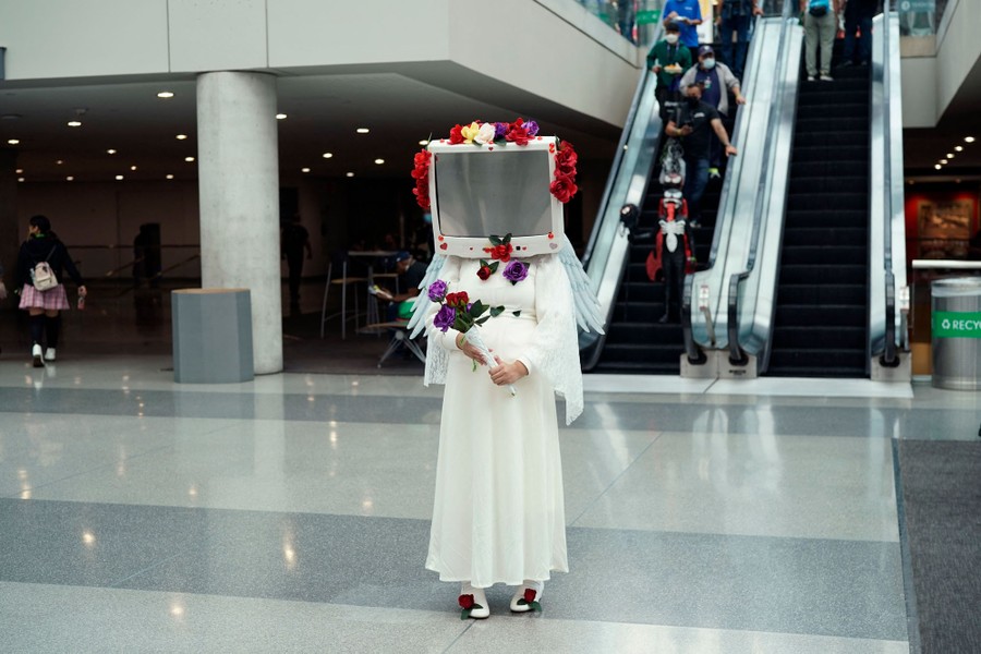 A costumed person with a television for a head stands in a lobby.