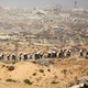 Men carry sacks of flour inside Gaza, where there are ruins in the background