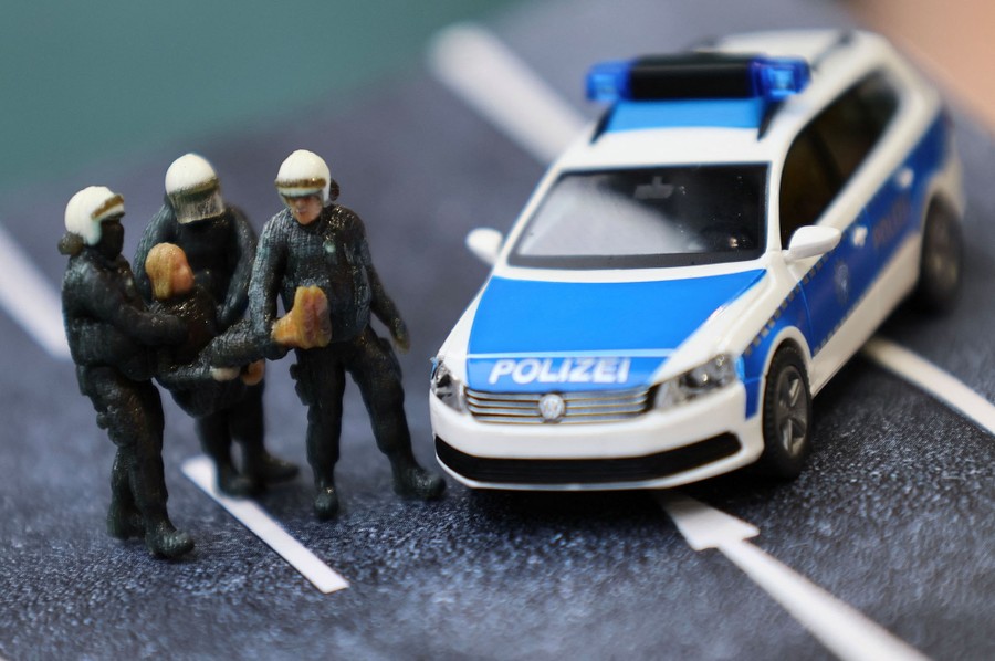 A close view of a small diorama with a toy car and three plastic police officers carrying a small plastic protester.