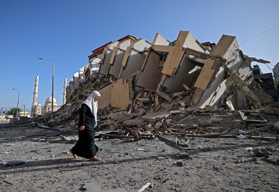 A woman walks beside the ruins of a fallen multistory building.