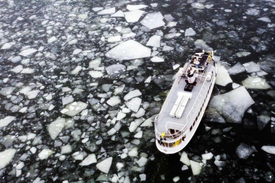 A boat moves through dark water, surrounded by small and large chucks of floating ice.