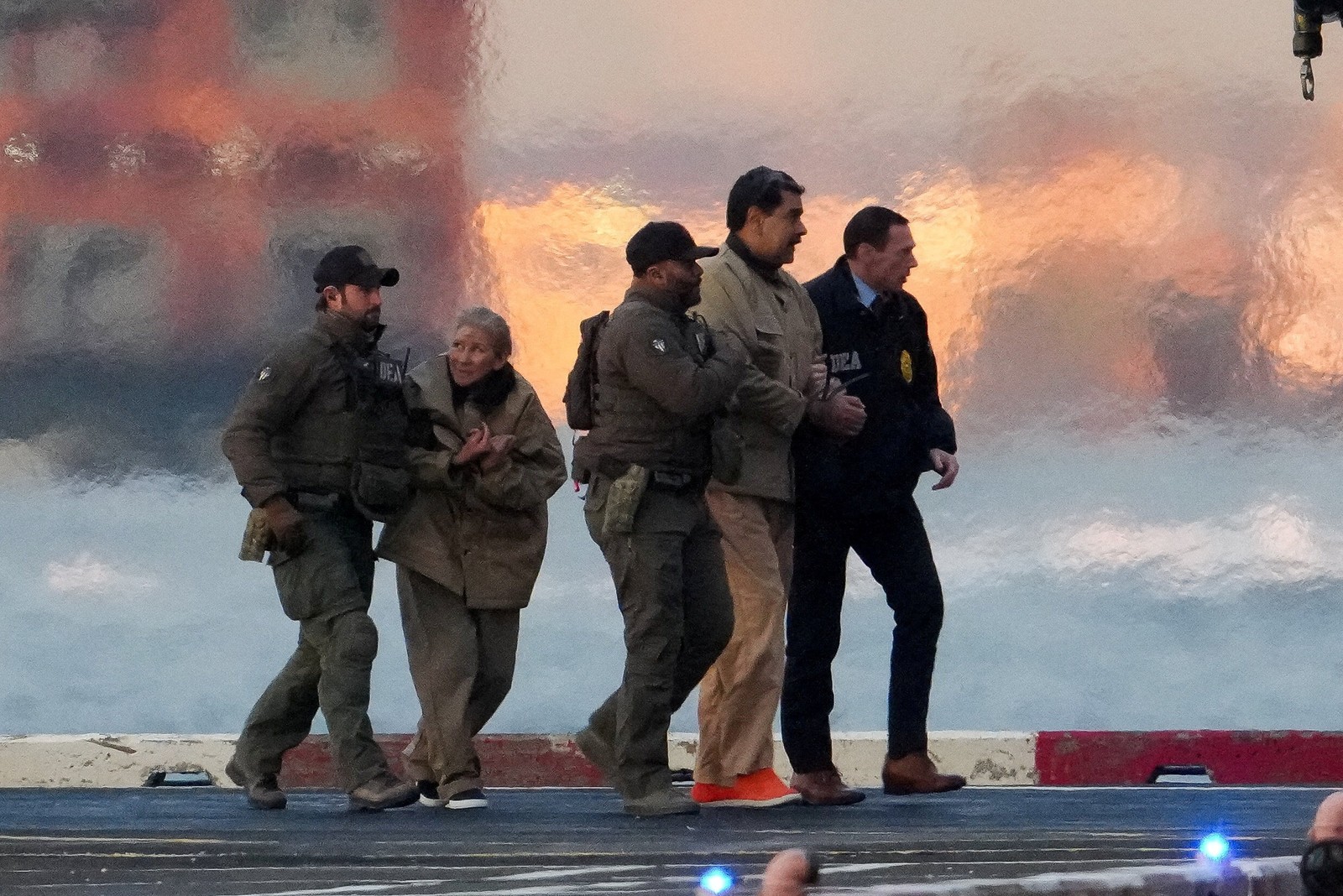 Several U.S. law-enforcement officers escort Venezuelan President Nicolás Maduro and his wife along a helicopter landing pad.