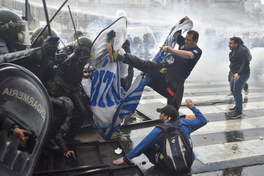 Several protesters kick at the shields of a group of riot police who push back.