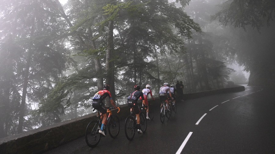 Cyclists ride through fog on a mountain road.