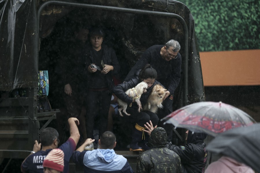 Several people and two small dogs are helped off the back of a truck during a rainstorm.