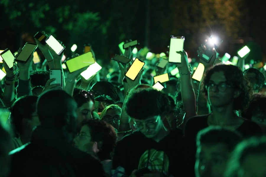 A crowd holds up many smartphones with green-colored sceens.